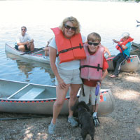 woman and boy wearing life jackets standing in front of canoes