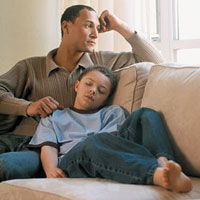 Man gazing out window with young son sleeping next to him on couch