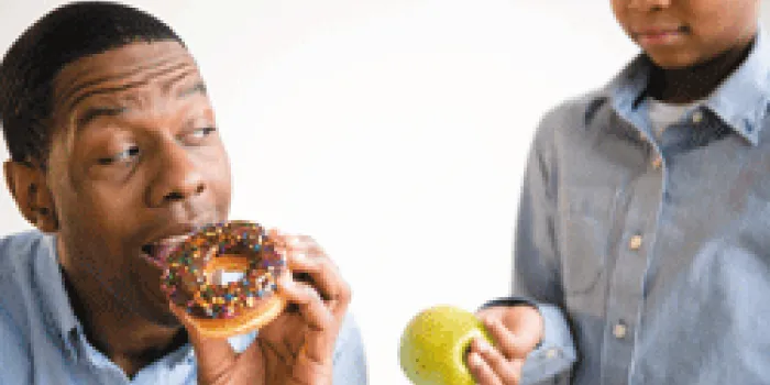Boy handing an apple to man about to eat a donut